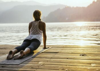 Beautiful woman practicing Yoga by the lake - Sun salutation series - Upward facing dog - Toned image