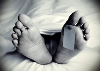 closeup of the feet of a dead body covered with a sheet, with a blank tag tied on the big toe of his left foot, in monochrome, with a vignette added